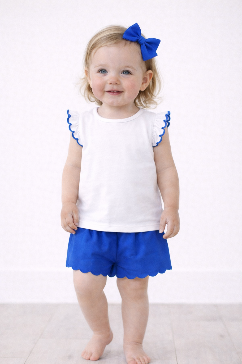 Young girl wearing a white top with blue ruffles and matching shorts on a white background